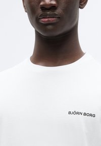 Λευκό βαμβακερό μπλουζάκι με στρογγυλή λαιμόκοψη, με μαύρο λογότυπο "BJÖRN BORG" στο αριστερό μέρος του στήθους. Λείο υφή.