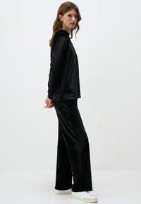Set di abbigliamento da casa nero realizzato in tessuto morbido e liscio; comprende una maglia a maniche lunghe e pantaloni larghi con una vestibilità comoda e design minimal.