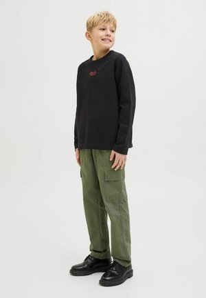 Chemise noire à manches longues avec un petit logo rouge, associée à un pantalon cargo vert olive avec plusieurs poches et des chaussures noires à lacets.