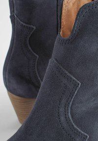 Bocanci ankle din suede bleumarin, cu un accent din piele maro, care prezintă detalii cusute și un toc din lemn.