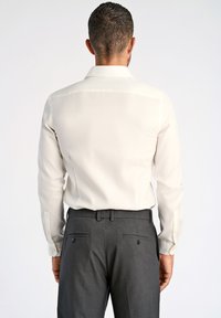 Camicia button-up chiara con una texture liscia, abbinata a pantaloni grigi scuri su misura con tasche posteriori e bottoni.