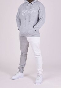 Sudadera gris con logo blanco, jeans de bloques de color gris y blanco, y zapatillas blancas. Diseño casual, textura suave y ajuste relajado.