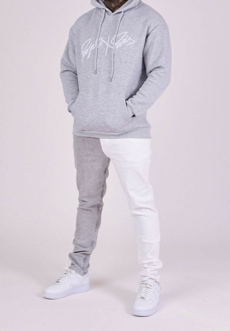 Sudadera gris con logo blanco, jeans de bloques de color gris y blanco, y zapatillas blancas. Diseño casual, textura suave y ajuste relajado.