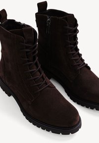 Braune Wildleder-Stiefeletten mit Schnürung an der Vorderseite, seitlichem Reißverschluss, robusten Gummisohlen und kontrastierenden Nähdetails.