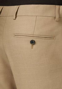 Beżowe spodnie wykonane z teksturowanej tkaniny, z jedną tylną kieszenią zapinaną na guzik oraz czystym, dopasowanym krojem.