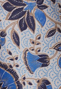 Motivo floreale blu e viola scuro con steli beige e sfondo puntinato azzurro chiaro su tessuto.