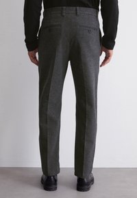 Pantaloni di lana grigia con una vestibilità sartoriale, caratterizzati da due tasche posteriori, passanti per cintura e una texture liscia, abbinati a calzature nere.