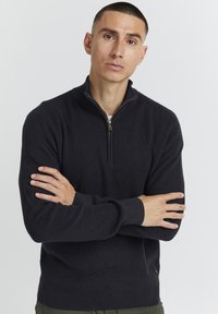 Pulover negru cu guler zip, texturat cu dungi, prezentând un fermoar mic și manșete strâmte. Construit dintr-un material moale și cald.