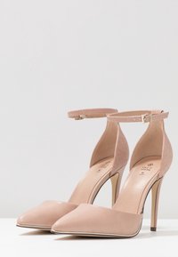 Zapatos de tacón desnudos con punta afilada y tira en el tobillo. Material de cuero suave con una tira texturizada y detalle de hebilla dorada.