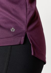 Lilla sportlik top tekstuurse mustriga, millel on küljes lõhik ja väike logo. Komplektis mustad retuusid.