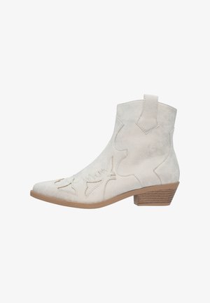 Bottine en daim blanc cassé avec des découpes de style western et un bout effilé. Dotée d'un talon empilé et de surpiqûres décoratives sur le côté.