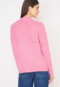 Różowy sweter dziewiarski z okrągłym dekoltem, prążkowanymi mankietami i dołem. Tekstura jest miękka i lekko fakturowana, z luźnym krojem.