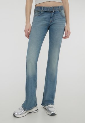 Jeans a campana di colore azzurro chiaro con design a cinque tasche e cuciture visibili. Presentano una cintura con una fibbia argentata. Texture in denim liscia.