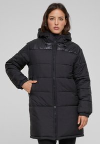 Abrigo acolchado negro con cierre de cremallera en la parte delantera, capucha y puños elásticos. Cuenta con un panel superior brillante, acolchado y bolsillos laterales.