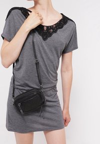 Szara sukienka z krótkim rękawem, z koronkowym wykończeniem wokół dekoltu, w połączeniu z małą czarną pikowaną torbą na ramie z zamkiem błyskawicznym.