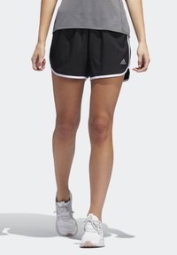 Pantalones cortos deportivos negros con ribetes blancos, hechos de material ligero, combinados con una camiseta deportiva gris y zapatillas blancas, mostrando un ajuste casual.
