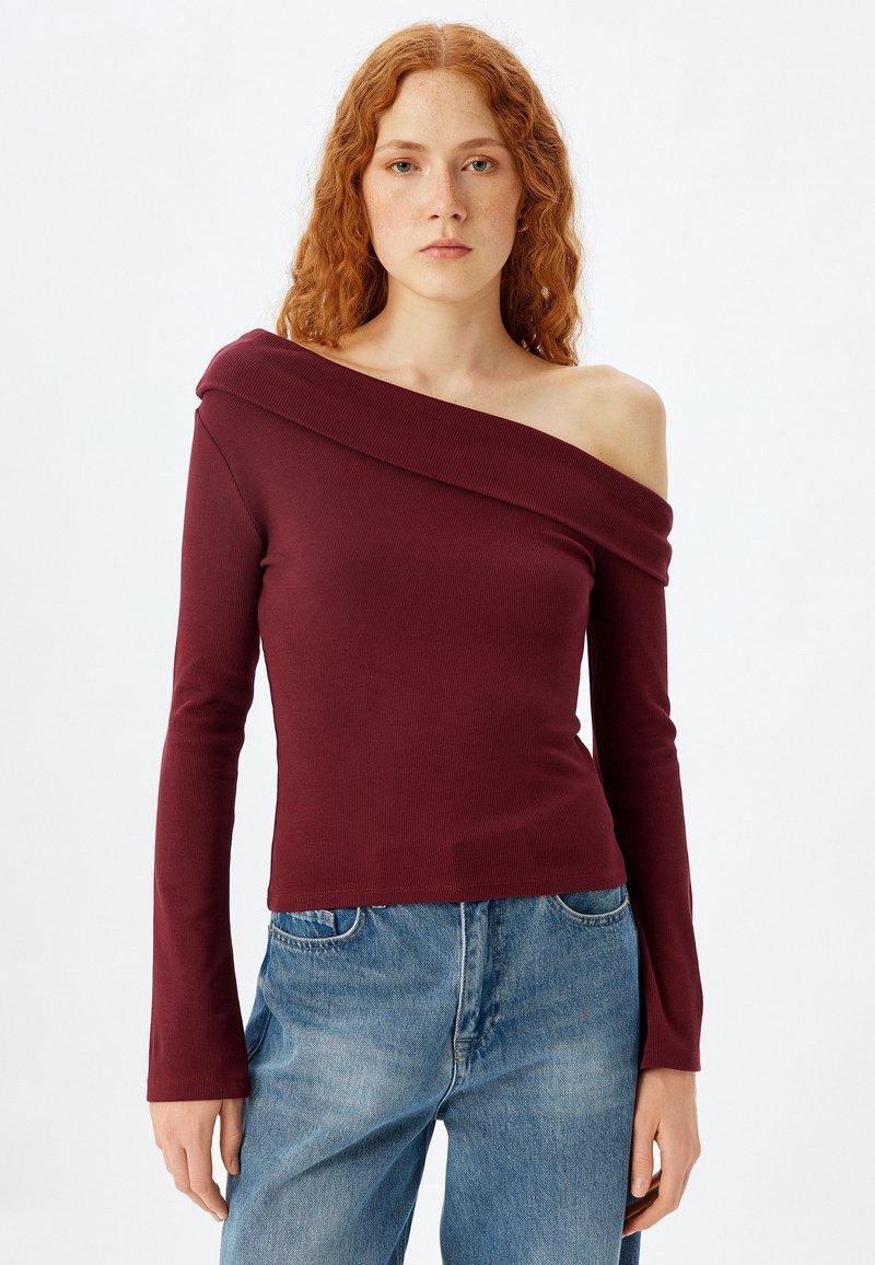 Burgunderfarbene Off-Shoulder-Bluse mit langen Ärmeln, gerippter Textur und figurbetontem Schnitt, kombiniert mit hellblauen Jeans.