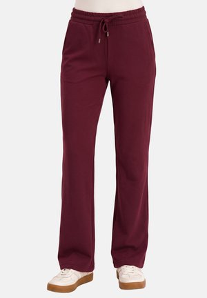 Bordeauxrode rechte broek met elastische tailleband en trekkoord, gedragen met witte sneakers met bruine zolen.