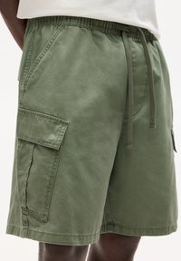 Shorts cargo verts en coton avec une taille élastique, plusieurs poches et une coupe décontractée. Le tissu a une texture lisse.