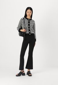 Svart och vit houndstooth-mönstrad cardigan med runda knappar, tillsammans med åtsittande svarta utsvängda byxor och svarta sandaletter med öppen tå.