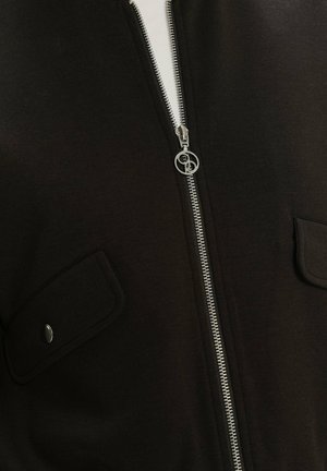 Čierna zipová bunda vyrobená z mäkkého materiálu, s strieborným zipsom a gombíkovými vreckami na hrudi. Hladký povrch s minimalistickým dizajnom.