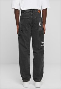 Pantaloni cargo in denim nero con ampie tasche posteriori e una patch con logo, dal fit rilassato e con orli risvoltabili.