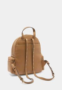 Zaino in pelle marrone con una forma arrotondata, numerose tasche con zip, cinturini borchiati e una maniglia superiore per il trasporto.