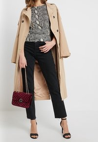 Beige trenchcoat lager över en topp med svart och vit ormtryck, i kombination med svarta jeans, svarta klackar och en borgundy kviltad handväska.