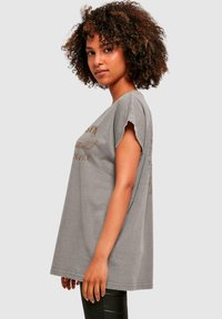 Grå oversized t-shirt lavet af bomuld, med rund halsudskæring, korte ærmer og trykt tekst i en kontrastfarve foran og bagpå.