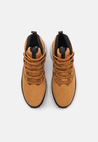 Bruna mockaskor för vandring med svarta detaljer, utrustade med en vadderad krage, texturerade snörningar och en vit gummisula.