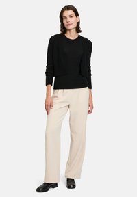 Gilet en tricot noir sur un haut noir, associé à un pantalon large beige clair et des chaussures en cuir noires. Design simple, texture douce.