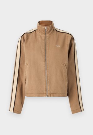 Hellbraune Zip-Jacke mit beigen und schwarzen Streifen auf den Ärmeln, hohem Kragen, Seitentaschen und kleinem weißen "obey"-Logo auf der Brust.