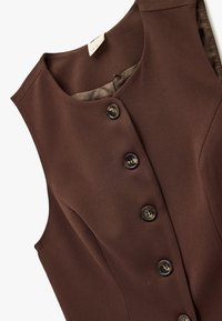 Vestido marrón sin mangas con una tela lisa y texturizada, cinco botones en la parte frontal y un escote redondeado con un forro interior de contraste.