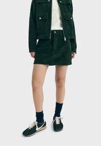 Mörkgrönt manchesterntyget jacka och kjolset med ribbad textur, kombinerat med svarta sneakers och marinblå strumpor. Kjolen har knappar och dragkedja fram.