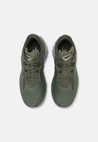 Chaussures de sport vertes avec une tige en maille, design perforé pour la ventilation et une semelle en caoutchouc grise. Présente des lacets et un logo de marque sur la languette.