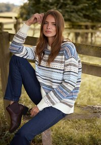 Sweter dzianinowy z wielokolorowymi geometrycznymi wzorami w niebieskim, białym i brązowym; połączony z ciemnymi dżinsami i brązowymi botkami za kostkę.