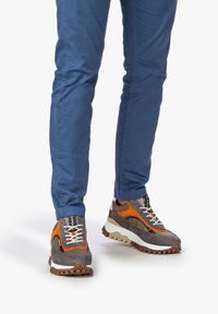 Le sneakers multicolori presentano una combinazione di suede e mesh grigio, con accenti arancioni, suola bianca, design di lacci texturizzati e suola in gomma sportiva.