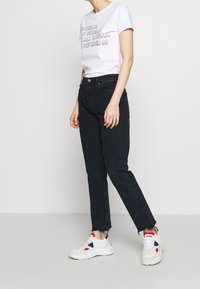 White t-shirt with text, dark skinny jeans, and chunky white sneakers with red and blue accents. Straight leg and raw hem detail on jeans.
