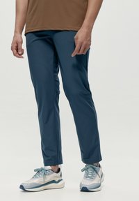 Modré športové nohavice s hladkou text�úrou, zúženým strihom a bočnými švami. Nosené s svetlosivými teniskami s modrými akcentmi.