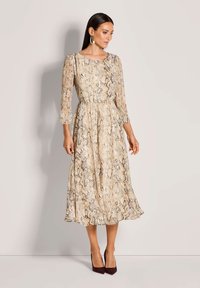 Ein knielanges Kleid mit Schlangenmotiv in Beige und Braun, mit Dreiviertelärmel, taillierter Passform und schwingendem Rock.