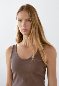 Bruine geribbelde tanktop met een ronde hals en dunne bandjes. De stof lijkt zacht met een gladde textuur.