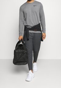 Szary longsleeve Nike, czarne spodnie z sznurkiem, białe trampki i czarna torba sportowa. Koszulka związana wokół talii.