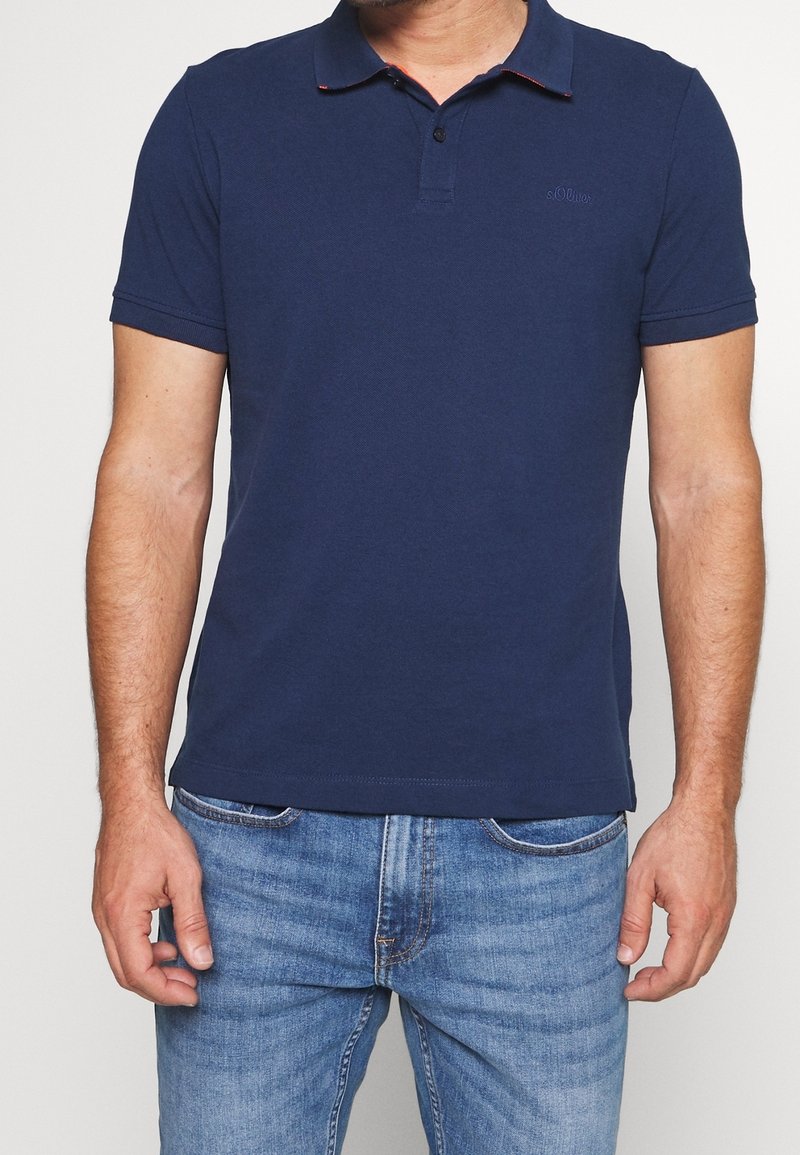 Polo shirt bleu marine en coton, avec un col à patte de boutonnage à trois boutons et de subtils accents rouges sur le bord du col.