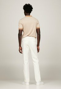Polo shirt striped beige da uomo con maniche corte, abbinato a pantaloni bianchi e sneakers bianche, visto da dietro.