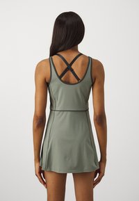 Vestido atlético verde com corpete ajustado e saia ampla. Apresenta alças cruzadas nas costas e costura em contraste. Tecido liso e elástico.