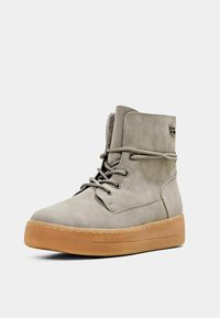 Bottine en daim gris avec un bout arrondi, un lacet à enfiler et une semelle en caoutchouc texturée couleur gomme. Présente des accents cousus et un talon renforcé.