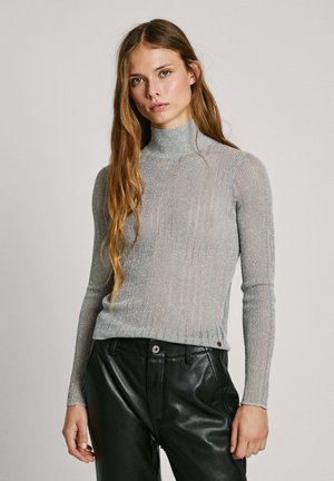 Lichtgrijze coltrui met een ribbelstructuur en metallic draadaccenten. Strakke pasvorm, lange mouwen, gecombineerd met zwarte leren broek.