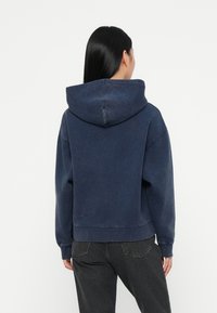 Marineblå cropped hettegenser med snøring, ribbede ermer og nederkant, laget av myk stoff med en lett slitt tekstur.