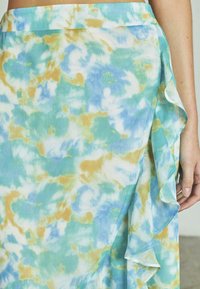Gonna leggera e fluida con un motivo multicolore di tonalità blu, verde e oro, con orlo arricciato e texture liscia.