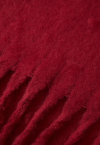 Tissu en laine rouge avec une surface douce et texturée, présentant des bords inégaux et des fibres visibles, ajoutant profondeur et détails au matériau.